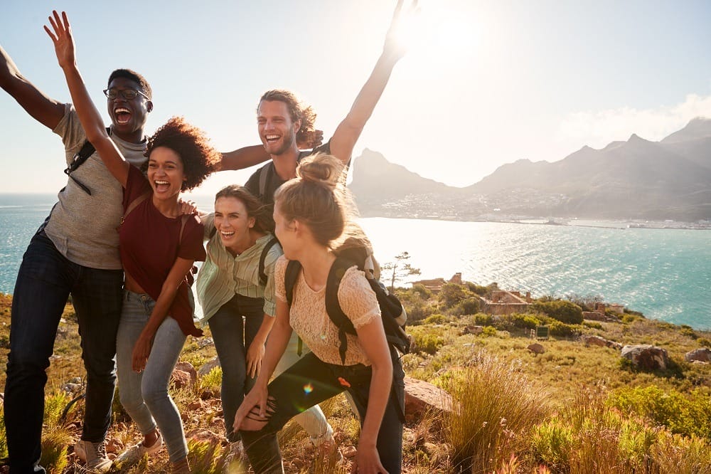 Millennial friends on a hiking trip celebrate reaching the summit and have fun posing for photos